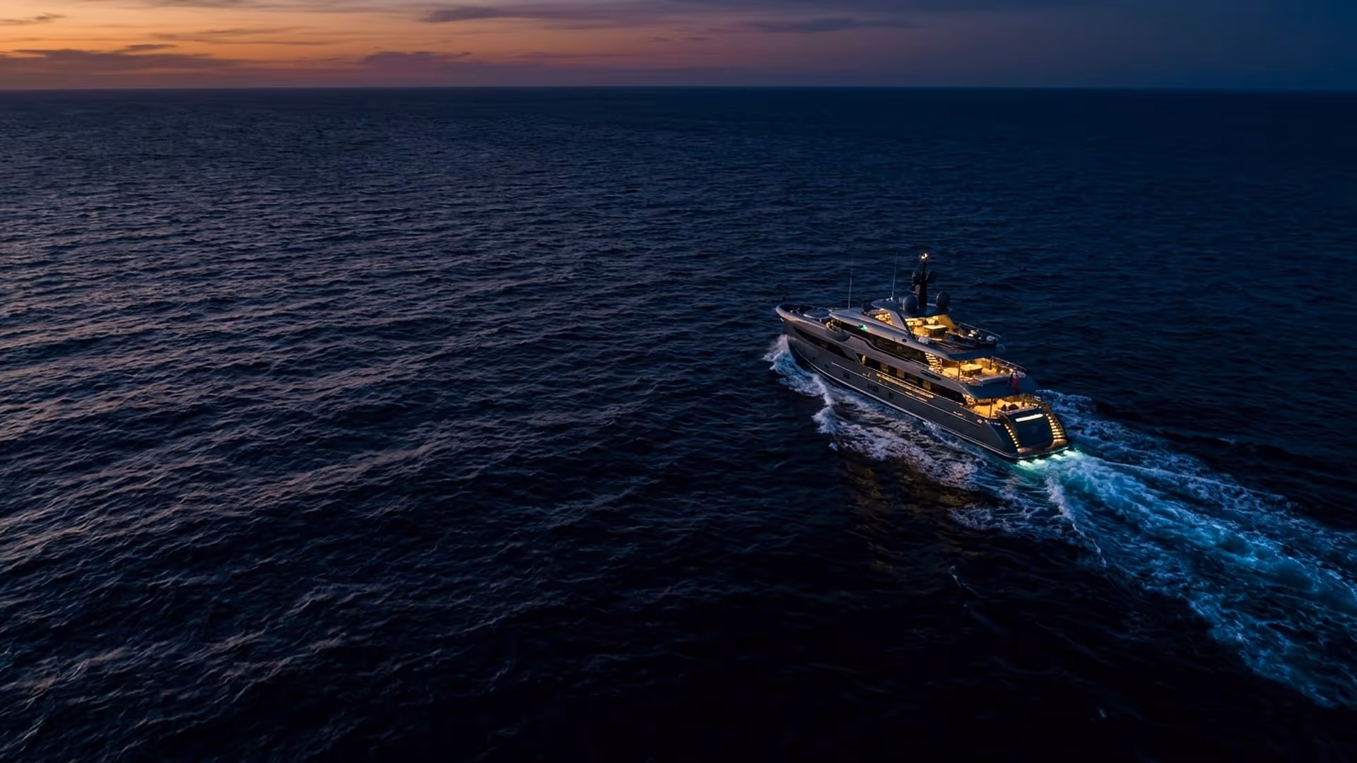 A modern expedition yacht cutting through dark open ocean at dusk, glowing wake trailing behind